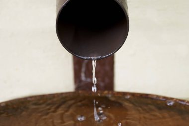 Yağmur suyu plastik bir drenaj borusundan metal varile akar.