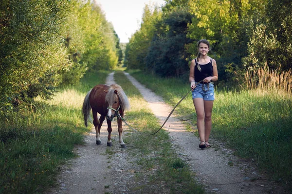 Nastolatka spacerująca z ogierkiem na smyczy wzdłuż wiejskiej drogi — Zdjęcie stockowe