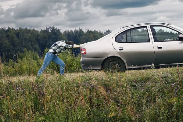 Mujer empujando su coche que se ha quedado sin gasolina a lo largo de un camino de campo — Foto de Stock