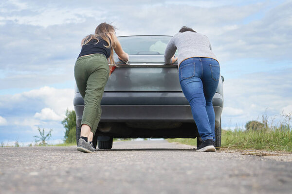 Two girls push their car which has run out of petrol along a country road