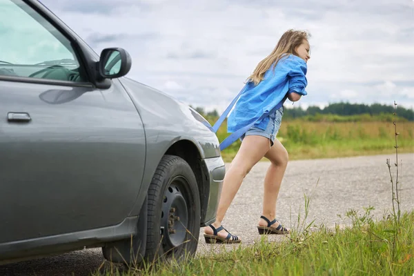 Teenage girl pushing her car which has run out of petrol along a country road — Stock Photo, Image