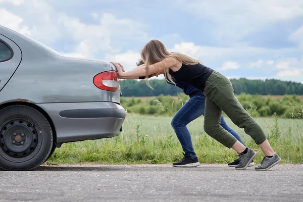 Две девушки толкают свою машину, у которой закончился бензин по проселочной дороге. — стоковое фото
