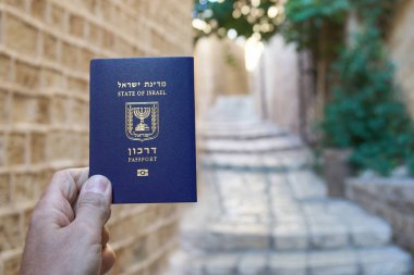 Erkek el, eski dar sokak arka planında İsrail pasaportu tutuyor.
