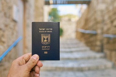 Erkek el, eski dar sokak arka planında İsrail pasaportu tutuyor.