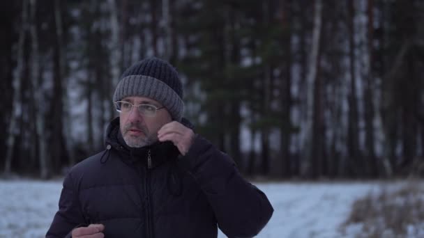 Hombre de mediana edad escucha la música en los auriculares en el campo en invierno — Vídeos de Stock