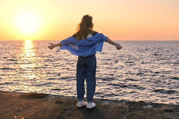 Happy Teenage girl standing with her hands outstretched on a sea pier at sunset