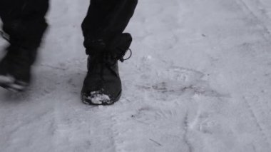 Feet of a man wearing black shoes freezing from the cold and shifting from foot to foot on the snow in winter. Man dancing trying to warm. 4K resolution video.