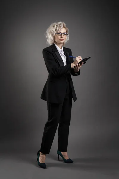 Jeune femme d'affaires blonde se tient dans un costume masculin dans des lunettes tenant un dossier noir ane écrit avec un stylo — Photo