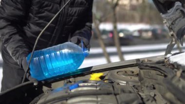 Man pouring an antifreeze liquid into a windshield washer tank of a car