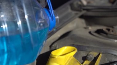 Filling up a windshield washer tank of a car by antifreeze close up