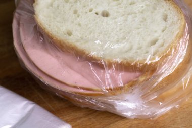 Kesme tahtasının üzerinde duran plastik torbada haşlanmış sosis dilimli sandviçler. Sandviçin yanında naylon poşetler vardı.