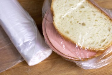 Kesme tahtasının üzerinde duran plastik torbada haşlanmış sosis dilimli sandviçler. Sandviçin yanında naylon poşetler vardı.