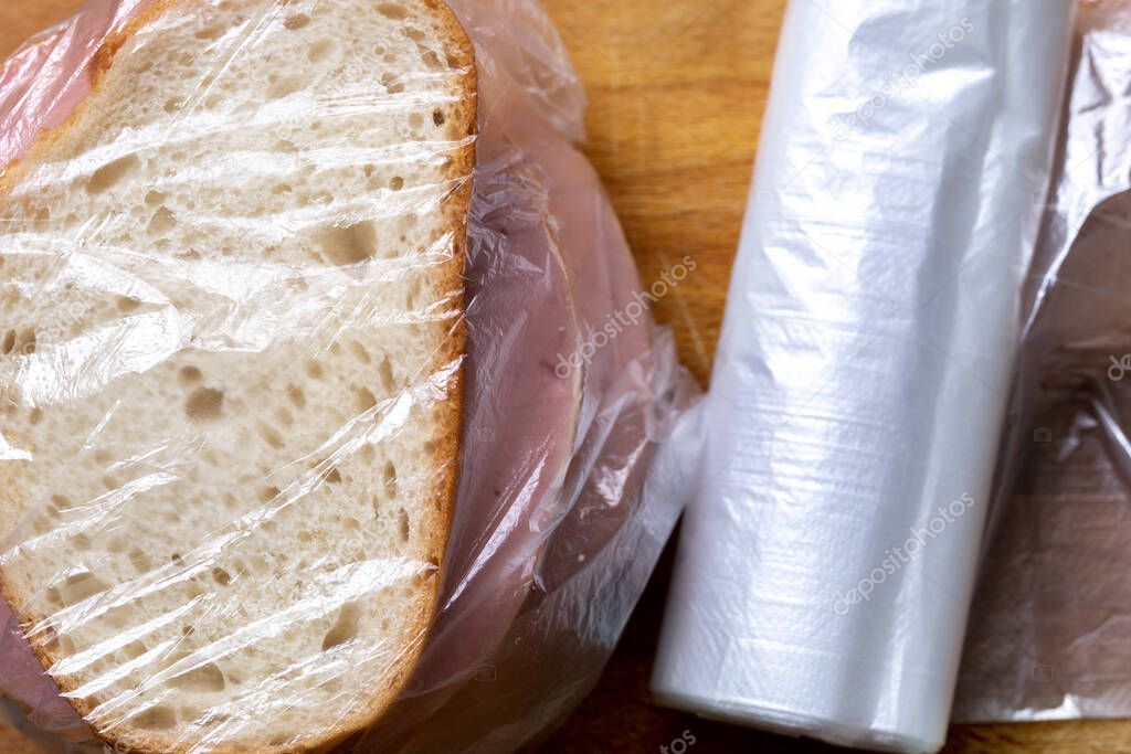 Sandwiches with slices of a boiled sausage in the plastic bag lying on the cutting board close up. Near a sandwich lying a roll of plastic bags