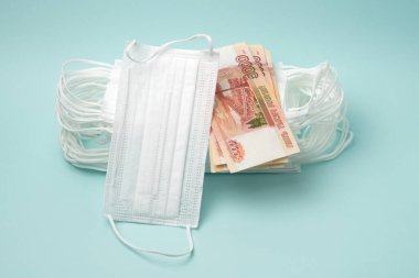 Mavi arka planda Rus parası olan bir yığın tıbbi maske. Rusya 'da koronavirüs salgınının yayılma korkusuyla ilgili olarak tıbbi maske fiyatlarının artması kavramı