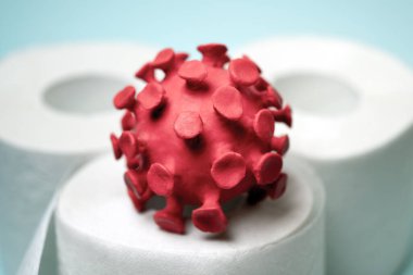 Tuvalet kağıdı rulosunun üzerinde oturan kırmızı koronavirüs modeli. Koronavirüs salgını sırasında panikle tuvalet kağıdı alma kavramı