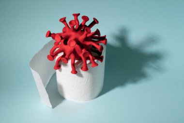 Tuvalet kağıdı rulosunun üzerinde oturan kırmızı koronavirüs modeli. Koronavirüs salgını sırasında panikle tuvalet kağıdı alma kavramı