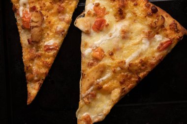 İki parça pizza, ev yapımı, siyah bir tepside yakın çekim.