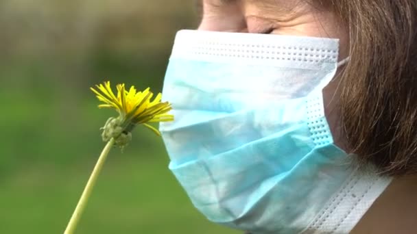 Mujer en máscara protectora médica huele un diente de león amarillo de cerca — Vídeo de stock