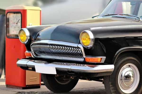 Frontal part of an old vintage black car near retro red gas station — Stock Photo, Image