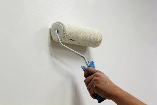 Mão do homem com uma pintura pincel rolo parede interior em branco — Fotografia de Stock