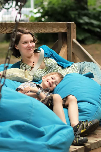 Moeder en zoon swingen op een enorme houten schommel met blauwe Boon zakken outdoors — Stockfoto
