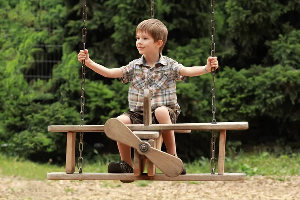 Five year old boy flying on a wooden plane swing in park — Stock Photo, Image