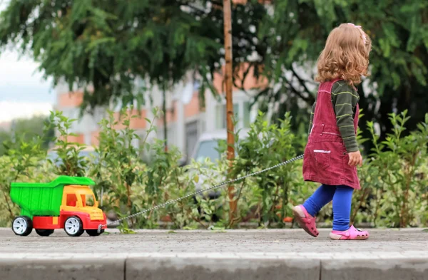 Ein Jahr altes lockiges Mädchen zieht einen großen bunten LKW — Stockfoto