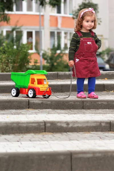 One year old girl with a big colorful truck trying to surmount an obstacle  of steps — Stock Photo, Image