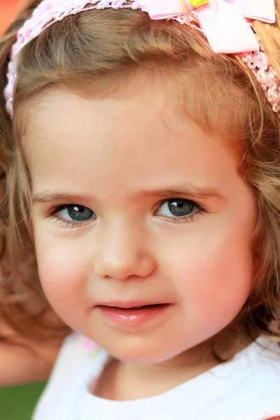 Närbild porträtt av en söt ett år gammal flicka med rosa huvudet band och en rosett, tittar rakt in i ögonen — Stockfoto