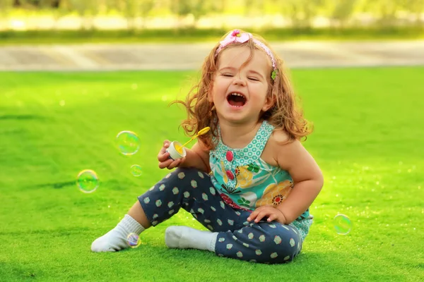 Lachen van één jaar oud meisje leren te blazen van zeepbellen en plezier op het gazon — Stockfoto
