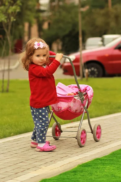 Retrato de una linda niña rizada de un año de edad con un paseo rosa juguete en el parque emulando a su madre —  Fotos de Stock