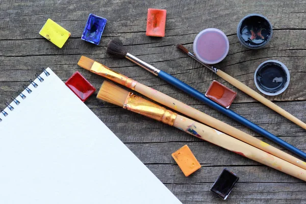 Platt layout av färgstarka akryl och akvarell färger, penslar och bundna vita album ark mock upp på grov grå träbord konsistens — Stockfoto