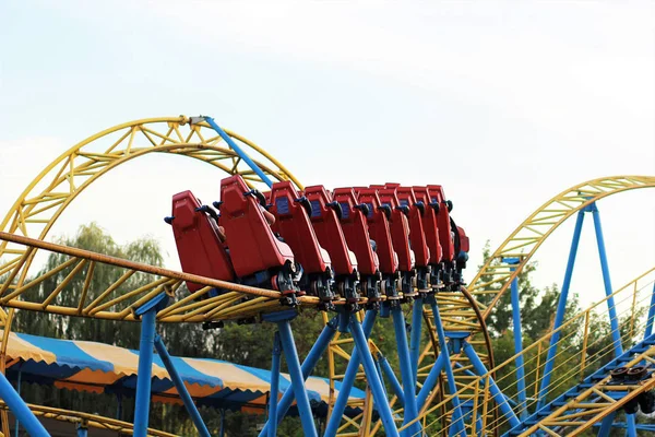 Kırmızı rollercoaster eğlence parkı içinde mavi gökyüzü mavi ve sarı demiryolu sürme — Stok fotoğraf