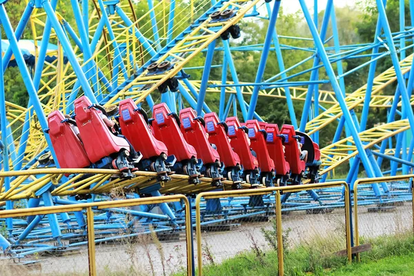 Czerwony rollercoaster jazda na niebieski i żółty kolejowe przeciw błękitne niebo w parku rozrywki — Zdjęcie stockowe