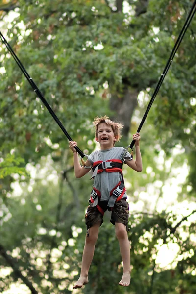 Boy jumping on a bungee trampoline and flying in the air in the summer park — Stock Photo, Image