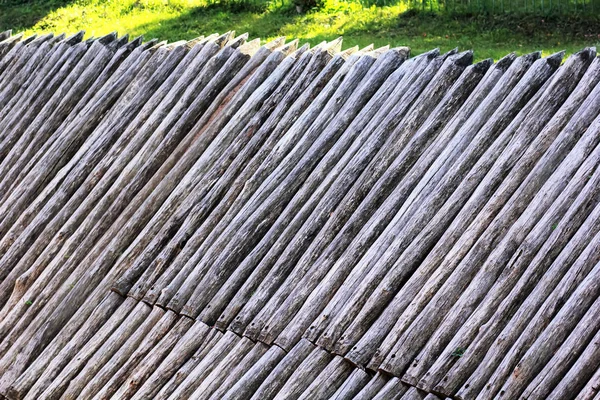 Grey ancient wooden palisade of the protective fence on the green lawn. Defensive stakewall