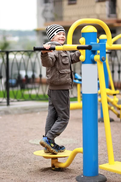 Vijf-jarige gelukkig jongen uit te werken in de straat, in de outdoor sportschool op de speelplaats. Jongen lachend, waardoor gezichten — Stockfoto