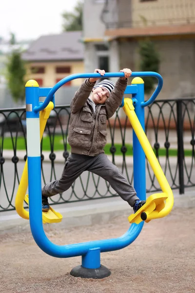 Vijf-jarige gelukkig jongen uit te werken in de straat, in de outdoor sportschool in de tuin op de speelplaats. Jongen lachend, waardoor gezichten. — Stockfoto