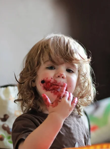 Baby meisje eten heerlijke bosbessen en zwarte bessen taart met haar gezicht vies helemaal. — Stockfoto