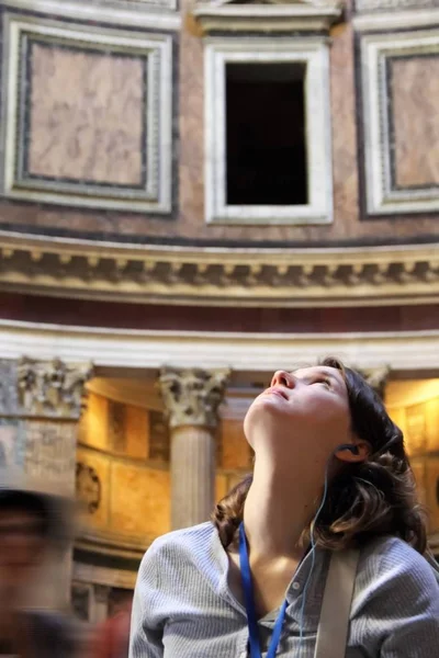 Young woman looking above and admiring the beauty of Pantheon in Rome, Italy. On excursion with audio guide and headphones