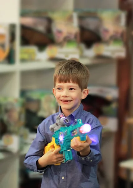 Feliz chico emocionado en una tienda departamental / centro comercial probando una pistola de juguete y eligiendo un regalo de Navidad. Viernes negro de compras . —  Fotos de Stock