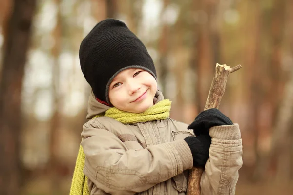 Portret van een lachende jongen in muts en sjaal in herfst park spelen met een stick-pistool. Onscherpe achtergrond — Stockfoto