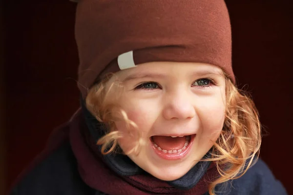 Close-up portret van een lachen één-jarige meisje van de baby in bruin hoed jas en sjaal tegen de donkere achtergrond op een warme dag — Stockfoto