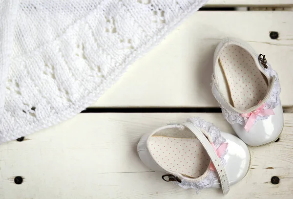 Flad lå af dejlig hvid vintage laklæder baby sko med lyserøde buer og snørebånd stående og hvid hånd lavet strikket cardigan på gamle hvidmalede træplanker . - Stock-foto