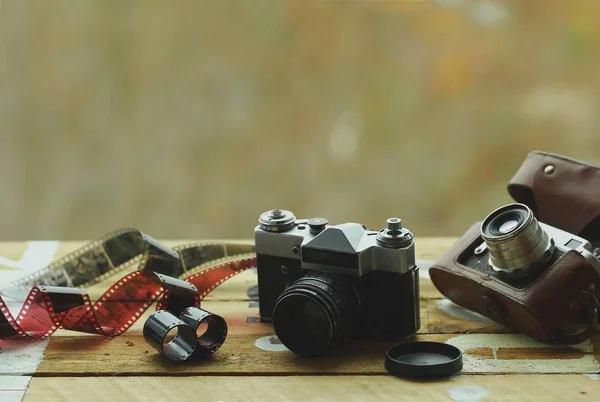 Due fotocamere vintage old school e pellicole sparse sul tavolo marrone chiaro. Uno in custodia retrò marrone. Sfondo sfocato — Foto Stock