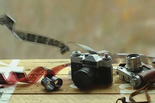 Deux appareils photo vintage de la vieille école et des films éparpillés sur table marron clair. Un en cuir brun rétro porte-étui un autre avec lentille fermée. Fond flou — Photo