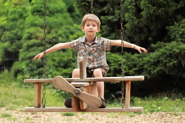 Pięcioletni chłopiec latający na płaszczyźnie drewniana huśtawka w parku lato — Zdjęcie stockowe