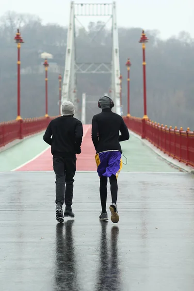 Dois afro-americanos jogging homens em um dia nebuloso chuvoso no centro da cidade de Kiev Pedestre ponte da cidade — Fotografia de Stock