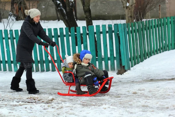 Mother is driving a sledge with two children in a snowy ukrainian village