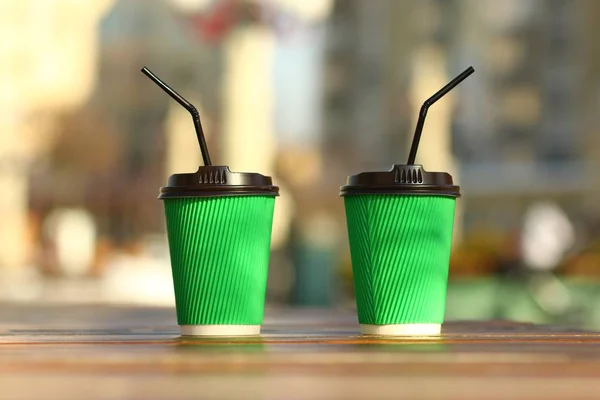 Closeup of green paper coffee cups on the outdoor wooden surface, place for logo, mockup, straws looking different direction